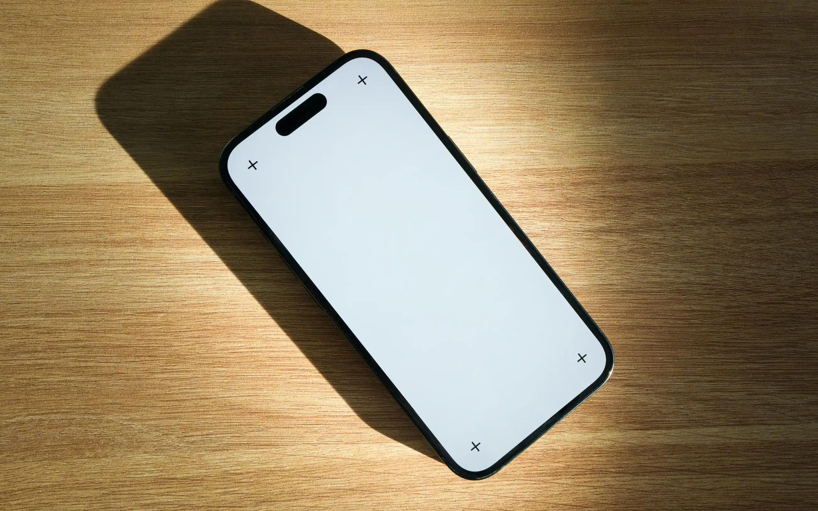 Mobitel s praznim zaslonom na drvenom stolu, u kosom svjetlu